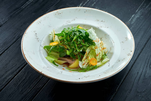 istock Appetizing, dietary salad with arugula, sauce, lettuce and warm beef in a white plate on a dark wood background. Healthy food 1308147704