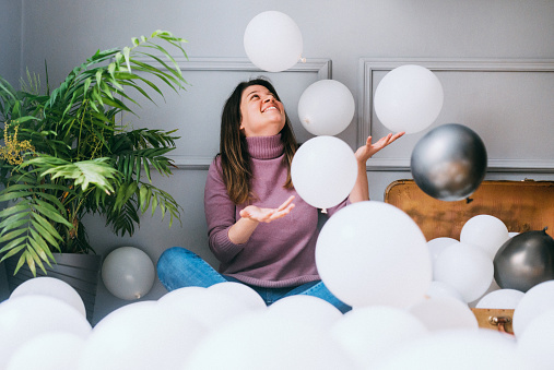 Young woman playing surrounded by balloons over gray background