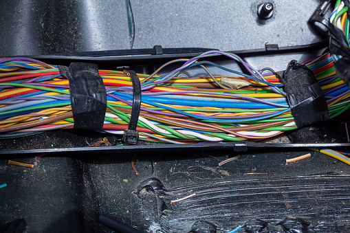 A bunch of dusty multi-colored electrical wires underneath the car's upholstery. Search and repair of a malfunction in a car service