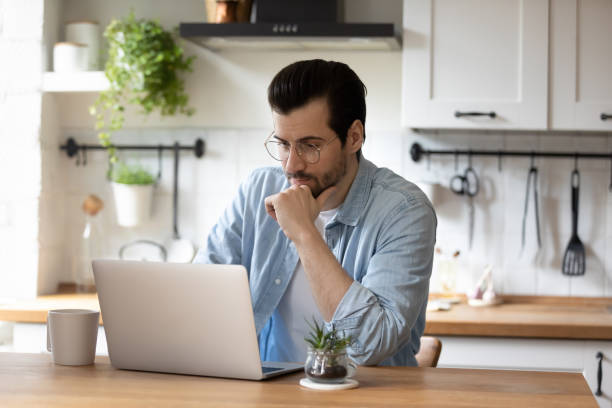 istock Pensive young man work on laptop at home kitchen 1308167433