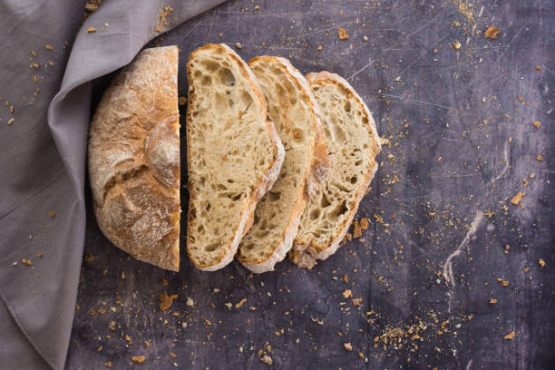istock Zenithal image of an ecological rustic bread divided into half slices on a dark surface surrounded by crumbs and a gray cloth 1308169646