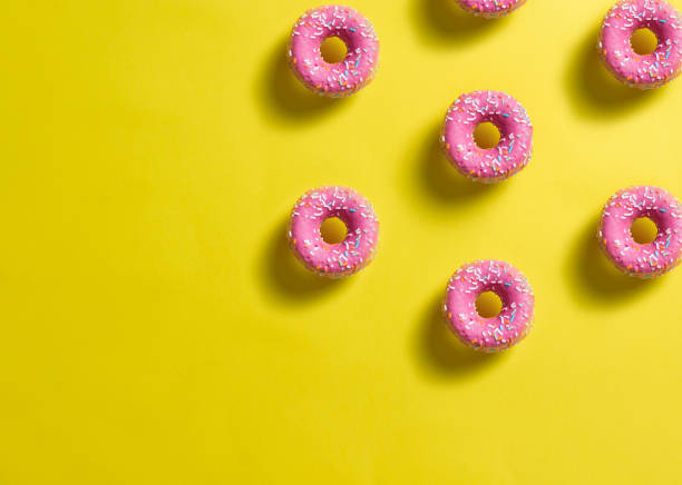 istock pattern of pink donuts decorated with colored confetti with shadow on lemon yellow background 1308169713