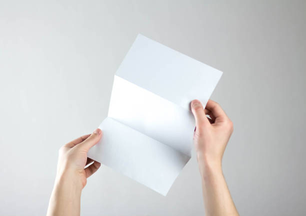 istock Hands hold a white three fold flyer. A clean flyer in your hands. For your text. Isolated on a gray background 1308176404