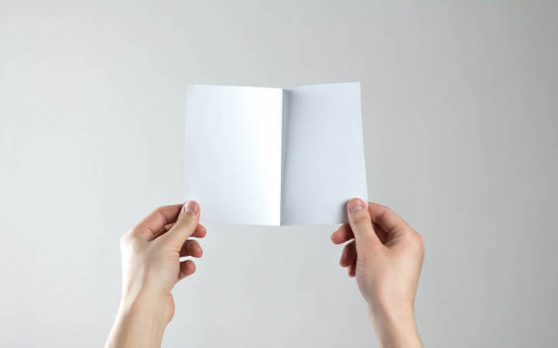 istock Hands holding a white folding flyer. A clean flyer in your hands. For your text. Isolated on a gray background 1308176406