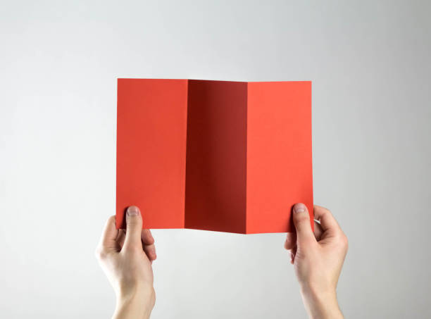 istock Hands hold a red three fold flyer. A clean flyer in your hands. For your text. Isolated on a gray background 1308176407