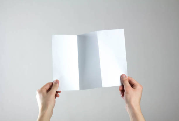 istock Hands hold a white three fold flyer. A clean flyer in your hands. For your text. Isolated on a gray background 1308176416