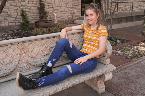 Confident pre-teen girl sits on a bench in modern ripped jeans. Copy space