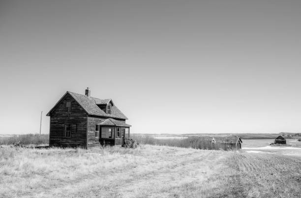 A beautiful two story farm house abandoned in an agricultural field in a black and white summer landscape