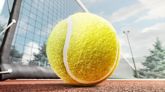 Vibrant yellow green tennis ball resting on a rustic clay court. This sports image captures the essence of tennis match on clay surface. Copy space.