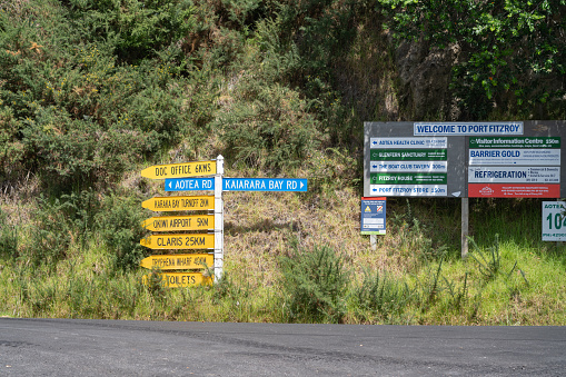 Great Barrier Island New Zealand - February 22 2021; Signpost with multiple destinations and distances near welcome and advertising sign at Port Fitzroy