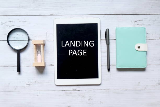istock Top view of magnifying glass,hourglass,pen,notebook, and tablet computer written ' LANDING PAGE' on white wooden backrgound. 1308178672
