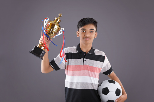 Portrait of Indian school boy holding a golden trophy cup with football