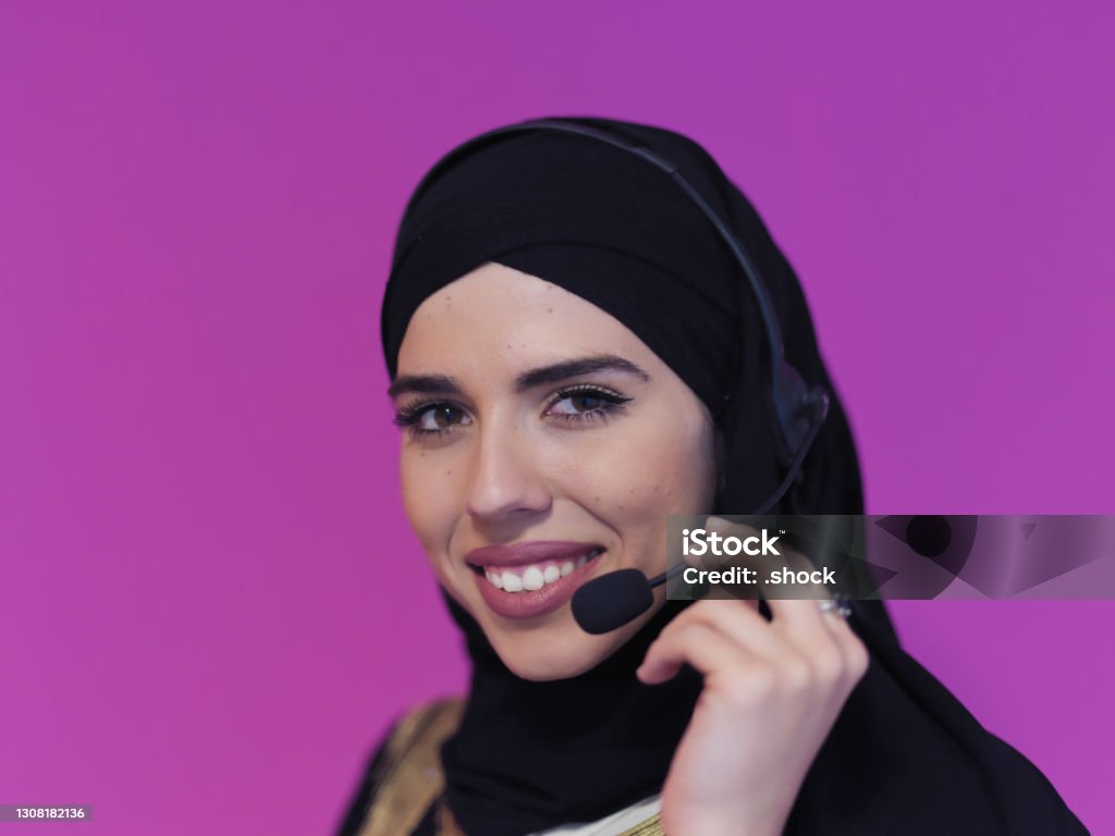 Portrait of young muslim woman with headphones Portrait of young muslim woman with headphones working as call center operator isolated on pink background Abaya - Clothing Stock Photo