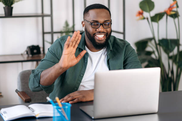 istock Online video communication. Happy smiling African American guy, freelancer or student, waving hand, greeting colleague, uses laptop for video conference with coworkers, telecommunication concept 1308182228