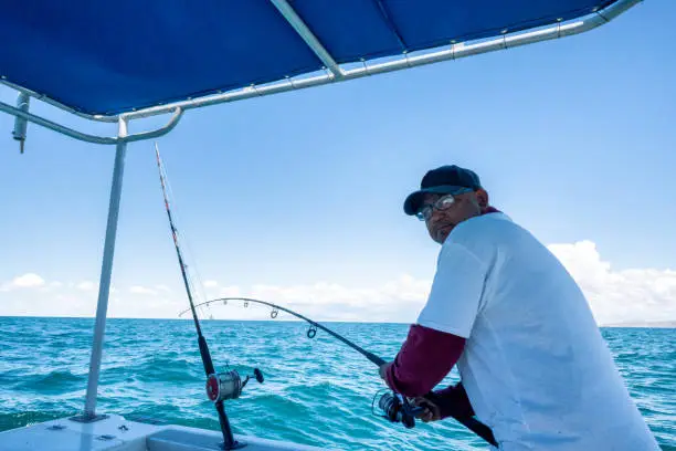 The Boat Captain Of A Fishing Charter In Puerto Penasco, Mexico, Reeling In A Fish On The Sea Of Cortez