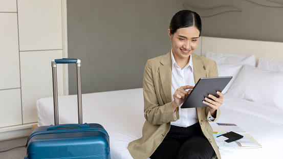 Young attractive female traveler using tablet to get information for her direction or place for dining around. Smiling young visitor checking news or business messages online in a clean apartment room