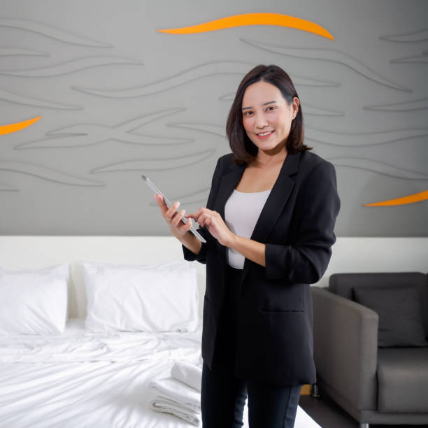 タブレットコンピュータを手に立つ黒いスーツを着たアジアのビジネスウーマン。ホテルのマネージャーは、ホテルのゲストのための部屋の整向性を確認します。 - bedroom hotel hotel room inn ストックフォトと画像