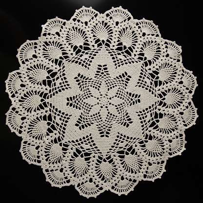 lace napkin made of beige threads on a black background, crocheted, handmade