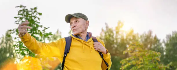 Elderly man wearing cap and backpack return and calling friends. Concept hiking exercises.