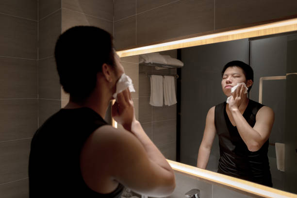 giovane asiatico che si lava il viso con un piccolo asciugamano davanti allo specchio - panno per il viso foto e immagini stock