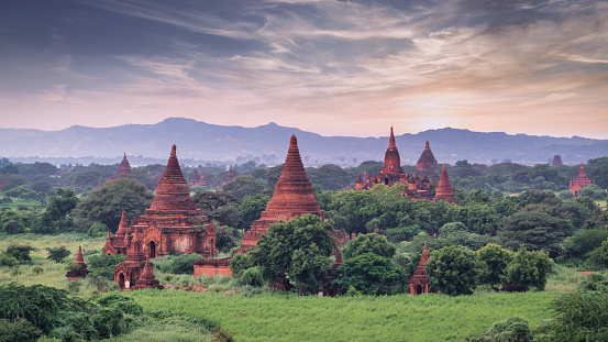 Beautiful sunrise over majestic buddhist temple pagodas in the ancient city of Bagan. View from above temple pagoda towards the horizon over ancient temple pagodas in between green tropical landscape after sunrise. Bagan, Mandalay Region, Myanmar - Burma, Southeast Asia, Asia.