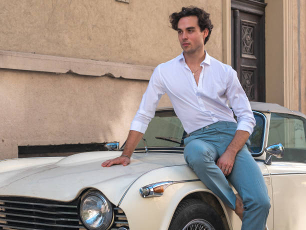 istock Attractive, handsome man leaning on a retro car in a white shirt. 1308215364