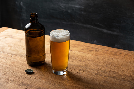 Bottle and glass of beer on a wooden table with dark background