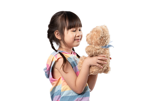 Cute little Asian girl hugging her favourite brown teddy bear and smiling in white background.