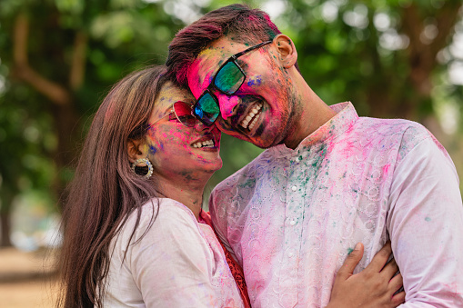 Closeup portrait of Young Indian Couple soiled with colorful bright colors or Gulal and Enjoying Holi Festival.