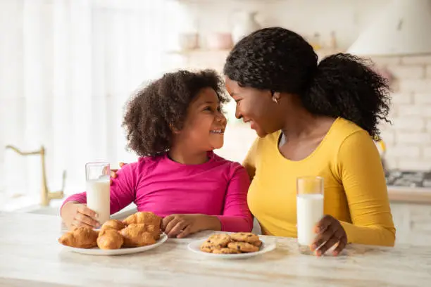 Photo of Happy Black Mother And Daughter Bonding Together While Having Snacks In Kitchen