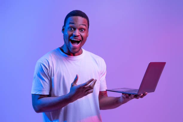 istock Cool Website. Excited Black Man With Laptop In Hands Under Neon Lighting 1308228404