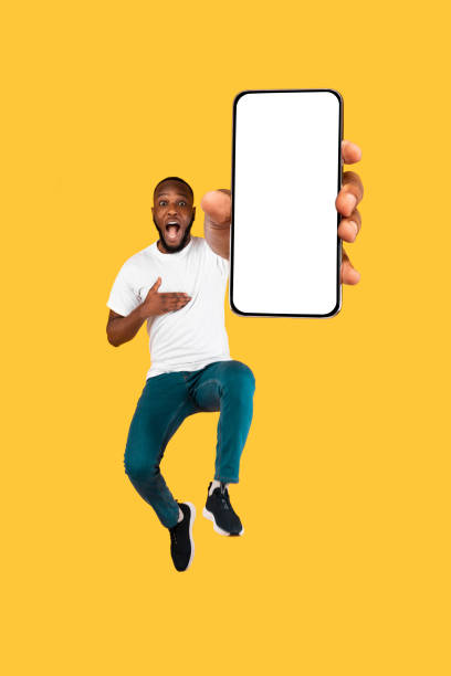 istock Black Guy Showing Phone Screen Jumping Posing Over Yellow Background 1308230653