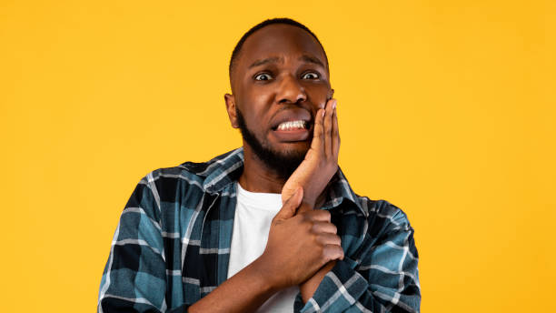 scared black guy touching cheek mit zahnschmerzen über gelbem hintergrund - abszess stock-fotos und bilder