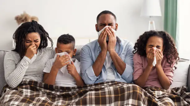 Photo of Sick black family blowing runny noses with napkins together