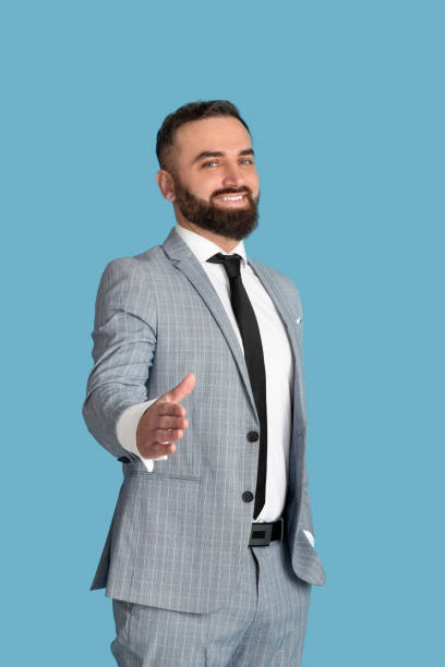 istock Successful millennial businessman offering his hand for handshake over blue studio background 1308232199