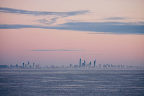 Horizontal landscape of the Gold Coast city buildings in silhouette on the far horizon with the pacific Ocean in the foreground and a sunrise pink sky above.