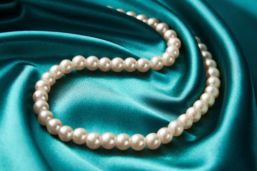Pearl necklace on green background, close-up. Luxury female jewelry,