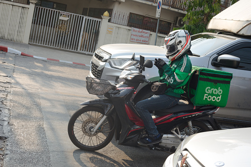Thai Grab Food delivery service person on motorcycle is standing in queue of traffic at traffic light in Bangkok Ladprao. Grab Food is one of booming deliver services in Bangkok during covid19 pandemic