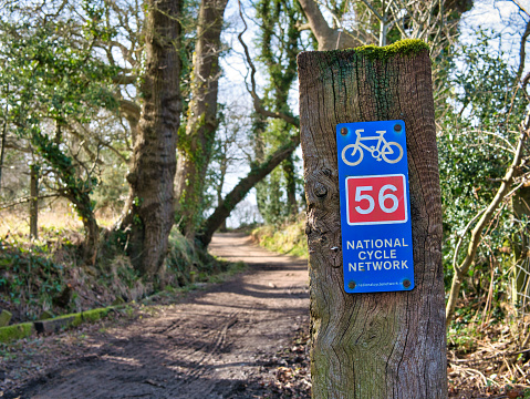 A blue metal sign on a wooden post shows the route of UK National Cycle Network route 56. Taken on a sunny day in winter in countryside Wirral in the north west of the UK.