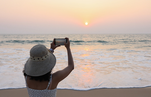 An Young Lady in Silhouette is seen Capturing the Panoramic Picture of the Sunset and its reflection upon the Sea at Padubidri Beach near Mangalore in Karnataka state,India.