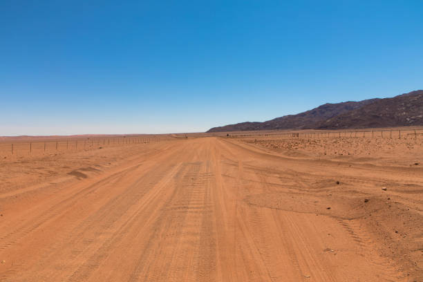 vista panoramica della strada dritta di ghiaia che attraversa il colorato deserto del namib, nel maestoso parco nazionale namib naukluft - dirt road road desert road gravel foto e immagini stock