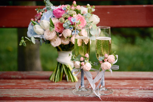 Sparkling wedding glasses with champagne and wedding bouquet on wood bench outdoors, copy space. Wedding concept