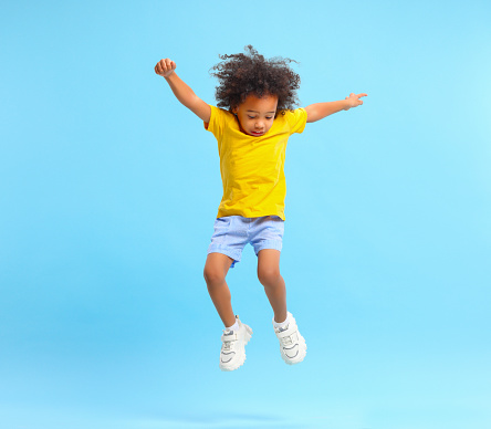 Active black kid jumping against blue background