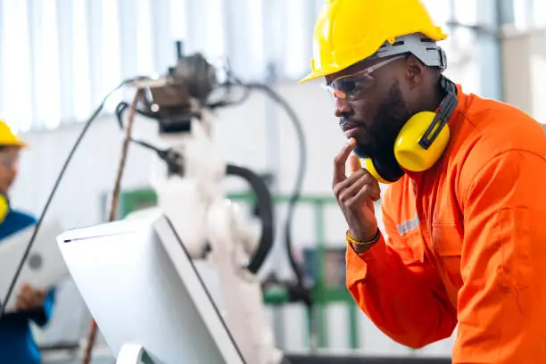 portrait of native american engineer technician wearing safty uniform hand contril automation robot arm welding machine with laptop industrial 4.0 factory background concept