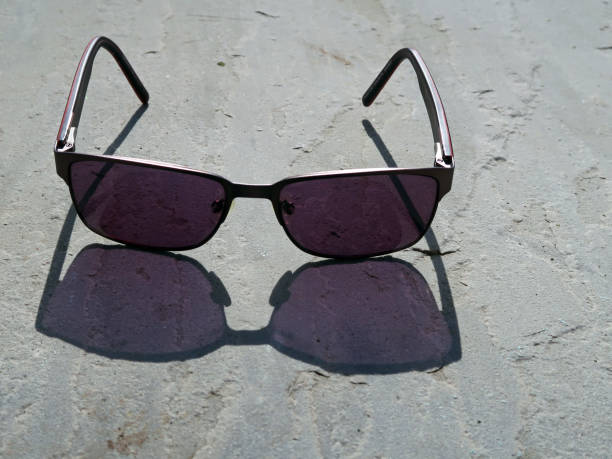 istock Pair of dark sunglasses in bright sunlight. Cast shadow on a light grey textured slate surface 1308248741