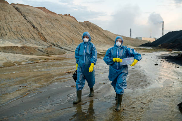 istock Two young female scientists in blue protective coveralls and rubber boots moving down polluted river 1308250757