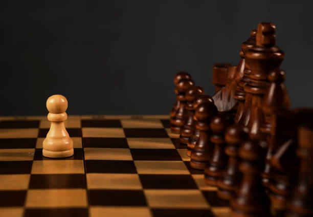 istock One white pawn against group of black chess figures on chessboard. Brave decisions concept 1308250845
