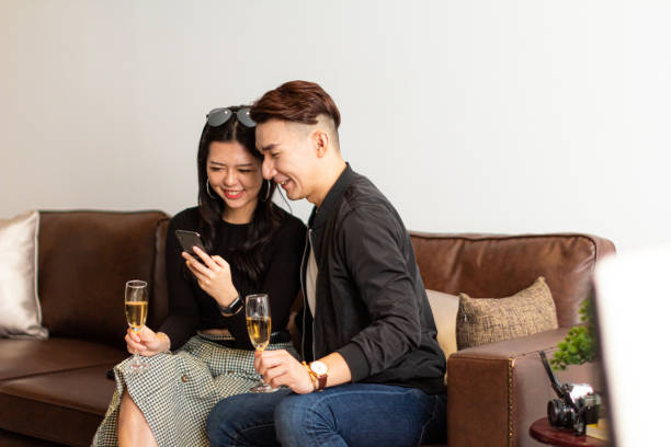 Asian Young Couple Enjoy Champagne Together On A Couch