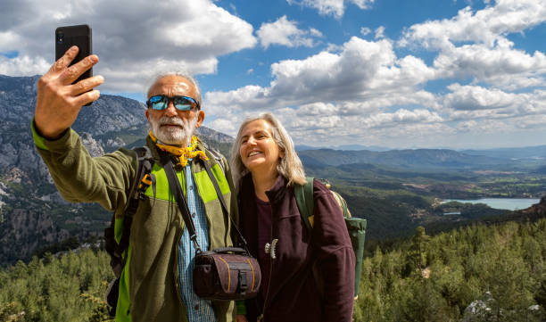elderly couple taking selfie in nature, against the landscape - senior adult mountain hiking recreational pursuit imagens e fotografias de stock