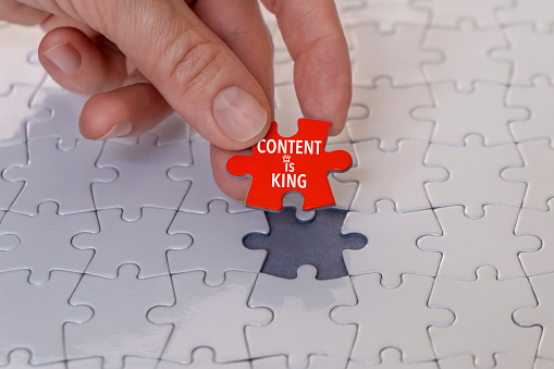 Businesswoman placing the last piece “Content is King” to complete the mission on the white puzzle background.